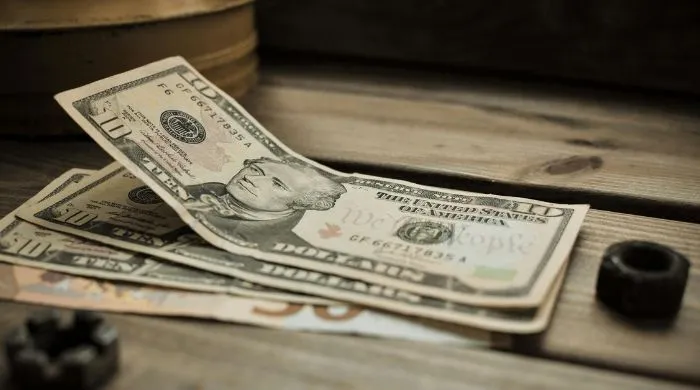 Stack of US dollar banknotes placed on a wooden surface, representing financial transactions and foreign exchange reserves amid Pakistan’s repayment of a $1 billion deposit to the UAE.