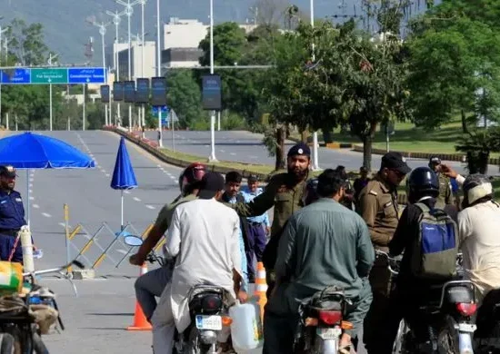 Police checkpoint in Islamabad with officers stopping motorcyclists at a barricaded road, reflecting strict security measures during the recent 12-day lockdown in the twin cities.