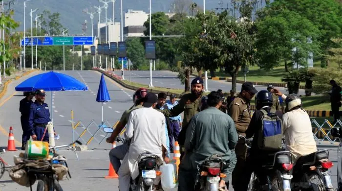 Police checkpoint in Islamabad with officers stopping motorcyclists at a barricaded road, reflecting strict security measures during the recent 12-day lockdown in the twin cities.