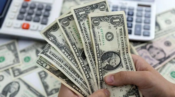 **Alt Text:** Hands holding US dollar banknotes with calculators in the background, representing the State Bank of Pakistan’s large-scale dollar purchases to strengthen foreign exchange reserves.